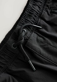 Black shorts with an elastic waistband, featuring a drawstring, smooth textured fabric, and contrasting stitching, focused on practicality.