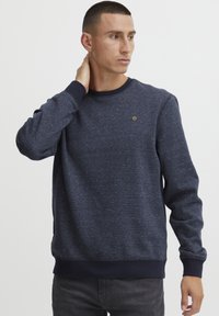 Donkerblauwe sweatshirt met een ronde hals, lange mouwen en geribde boorden. Beschikt over een subtiele textuur en een klein logo op de borst.