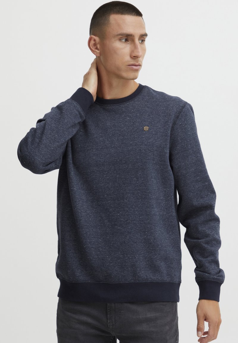 Donkerblauwe sweatshirt met een ronde hals, lange mouwen en geribde boorden. Beschikt over een subtiele textuur en een klein logo op de borst.