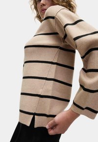 Beige randig tröja med svarta horisontella linjer. Långa, något puffiga ärmar och sidofickor vid fållen. Mjuk stickad textur.