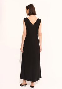Czarna, bezrękawnikowa sukienka maxi z głębokim dekoltem na plecach, wykonana z gładkiego materiału, o prostym kroju i subtelnym detalem markowym na plecach.