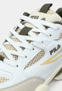 Λευκό και μπεζ αθλητικό παπούτσι με υλικά από δίχτυ και δέρμα. Διαθέτει κορδόνια, λογότυπο και μια λεπτή χρυσή λεπτομέρεια στο πλάι.