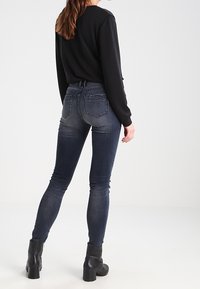 Mörkblå skinny jeans i denim, med bakfickor, subtila sömnadsdetaljer och midjehöjd, tillsammans med en svart topp och stövlar.
