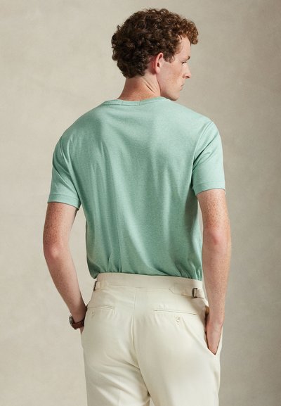 Krátké tričko světle mátové barvy s měkkým, texturovaným povrchem a volným střihem, doplněné béžovými kalhotami s pasem a zadními kapsami.