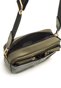 Bolso cruzado compacto en cuero verde oliva y negro. Cuenta con dos compartimentos con cremallera, herrajes dorados y una superficie texturizada.