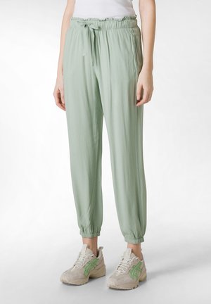 Pantaloni jogger verde chiaro con vita elastica, fondo a costine e tasche laterali. Indossati con sneakers beige con accenti verdi.