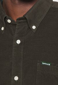 Dark green corduroy shirt with a button-down collar, white buttons, and a small green "Barbour" label on the chest pocket.
