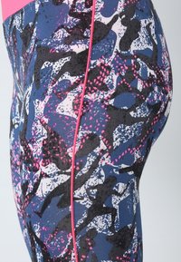 Leggings in una combinazione di colori blu navy e rosa, con un motivo astratto caratterizzato da silhouette nere e punti. Tessuto liscio e elasticizzato con rifiniture laterali rosa.