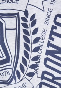 Camiseta de algodón blanca con estampado gráfico en azul marino. El diseño incluye un escudo, hojas de laurel y elementos de texto, con una textura suave.