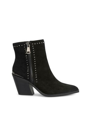 Bottines en daim noir avec un bout pointu, des clous argentés le long de la fermeture éclair, et un talon épais pour plus de stabilité.