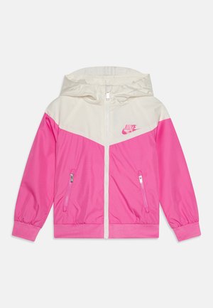Giacca windbreaker Nike con parte inferiore rosa e parte superiore crema, dotata di cappuccio, tasche con zip e logo a contrasto sul petto.