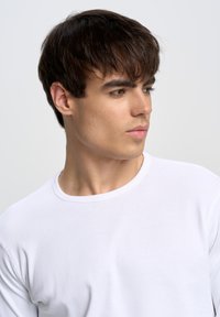 Hvid langærmet T-shirt med rund hals lavet af glat bomuldsstof; har et simpelt design uden mønstre eller detaljer.