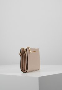 Beige leather wallet with gold hardware, two zip compartments, and a compact rectangular shape. Textured surface and minimal design details.