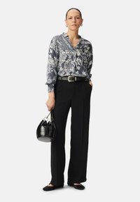 Blusa floreale navy con maniche lunghe, pantaloni neri a vita alta, cintura nera, borsa nera piccola e scarpe nere basse.