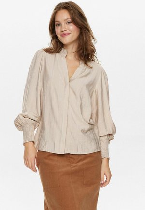 Collared, long-sleeve blouse in light beige with subtle vertical stripes, featuring elasticized cuffs and a loose fit. Worn over a brown skirt.
