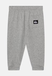 Grå sweatpants med dragsko i midjan, elastiska muddar och en bakficka med ett svart logopatch. Mjuk, strukturerad tyg.