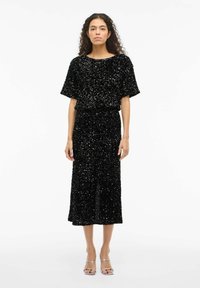 Robe midi noire à sequins avec une coupe décontractée, des manches courtes et un col rond, présentant une surface texturée et une taille cintrée.