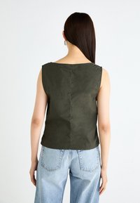 Olive green sleeveless top with a straight neckline, textured fabric, and a seam down the back. Worn with high-waisted light blue jeans.