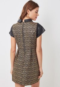 Vestido de patrón negro y dorado con una textura suave, mangas cortas y cierre en la parte posterior. Presenta un cuello redondeado y un corte entallado.
