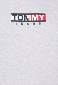 Szara bawełniana koszulka z nadrukiem "TOMMY" w pogrubionym czerwonym kolorze oraz "JEANS" w czerni na białym prostokącie, gładka tekstura i prosty design.
