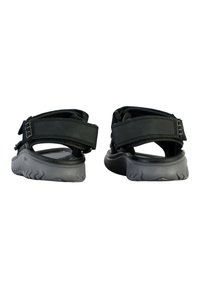 Sandalias negras con correas ajustables, una plantilla acolchada y una suela texturizada en gris. La vista trasera muestra dos correas y un diseño robusto.