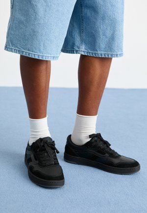 Black sneakers with suede and leather materials, featuring a lace-up design, contrasting stitching, and a textured rubber sole.