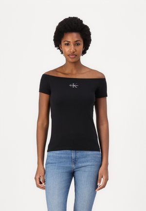 Čierne priliehavé tričko bez ramien, vyrobené z bavlny, s malým bielym logom Calvin Klein na hrudi, spárované so svetlo modrými džínami.