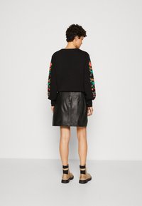 Sudadera negra con bordado floral Colorido en las mangas, combinada con una falda de cuero negra. La modelo lleva botas de tobillo color beige con correas.