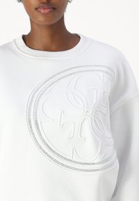 Felpa bianca con un design ricamato testurizzato e tonale in forma circolare, arricchito da cuciture decorative. Collo a girocollo, vestibilità rilassata.