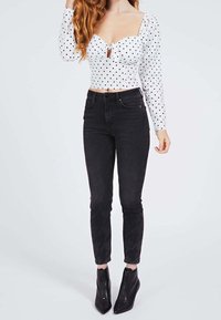 Crop top blanc à pois avec un décolleté carré et un détail œil-de-bœuf, associé à un jean skinny noir taille haute et des talons à fermeture éclair à la cheville.