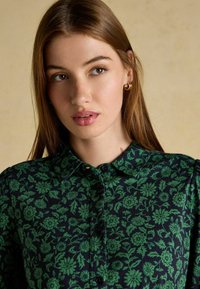 Tumesinine särk rohelise lillemustriga, nööbiväärise disainiga, kraedetailiga ja pehme tekstuuriga. Esiküljel on nööbid ja lilleaktsendid.