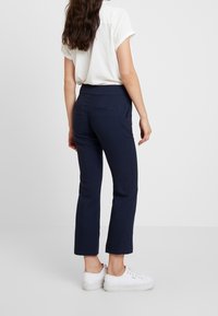 Námořnické kalhoty s přiléhavým pasem a rovnými nohavicemi, zdobené jemnou kostkovanou strukturou a dvěma zadními kapsami. Spárované s bílými teniskami.