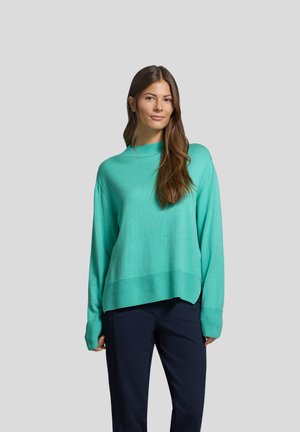 Helles Türkis oversized Pullover mit geripptem Ausschnitt und Bündchen, langen Ärmeln und geradem Saum. Kombiniert mit dunklen Hosen.