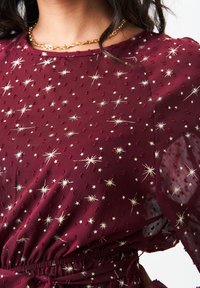 Burgundy dress featuring a sheer fabric with gold star and circle patterns, textured with raised dots, and an elastic waistline.