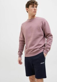 Lyserød sweatshirt med rund hals og ribkant, kombineret med marineblå shorts med hvid logo-broderi. Glat tekstur, afslappet design.