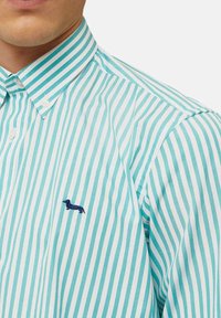 Overhemd met knopen in turquoise met witte strepen. Bevat een klein marineblauw geborduurd teckel logo op de linkerkant van de borst. Katoenen stof structuur.