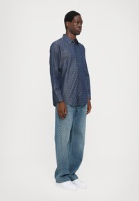 Camisa de manga larga azul marino con lunares blancos, cuello abotonado, combinada con jeans de pierna ancha azul claro y zapatillas blancas.
