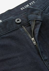 Jeans slim fit din denim albastru închis, cu fermoar YKK, cusături contrastante și un nasture metalic negru la talie.