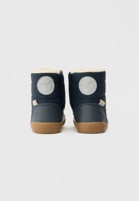 Sötétkék téli csizma bézs bolyhos béléssel, szürke textúrájú sarokkal, kerek logóval és világosbarna gumi talppal, hátulról mutatva.