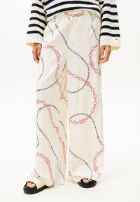 Pantaloni a gamba larga in tessuto color crema chiaro con un motivo a catena in rosso e nero. Presentano una vita elastica e un design fluido.