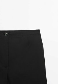 Ceinture de pantalon noir avec fermeture à bouton et couture visible sur fond blanc.