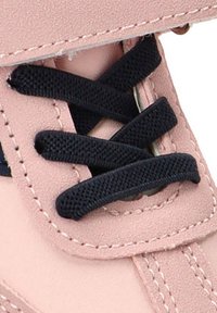 Primer plano de un zapato rosa pálido con cordones negros, material mate suave, ojales reforzados y costuras contrastantes a lo largo de los bordes.
