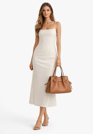 Woman wearing a white sleeveless midi dress and nude heels, holding a large brown leather tote bag with handles.