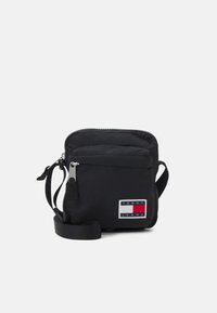 Czarna torba na ramię z nylonu z zamkiem błyskawicznym, z naszywką z logo Tommy Jeans w czerwonym, białym i niebieskim kolorze. Do torby dołączony jest regulowany pasek.