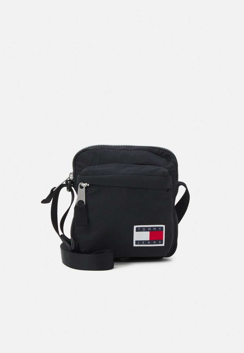 Czarna torba na ramię z nylonu z zamkiem błyskawicznym, z naszywką z logo Tommy Jeans w czerwonym, białym i niebieskim kolorze. Do torby dołączony jest regulowany pasek.