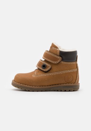 Botte en cuir marron avec deux bandes Velcro, doublure en fourrure blanche en haut, détails brodés, semelle en caoutchouc et un logo sur le côté.