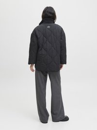 Veste matelassée noire avec un col haut et un motif texturé, associée à un pantalon gris ample et des chaussures noires, vue de dos.