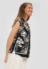 Schwarze ärmellose Bluse mit einem weißen floralen Muster, V-Ausschnitt und einem leicht lässigen Schnitt, aus leichtem Material gefertigt.