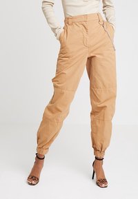 Pantalons cargo beiges avec un poignet élastique, des passants de ceinture et un détail en chaînage sur le côté ; fabriqués dans un tissu léger avec une coupe décontractée.