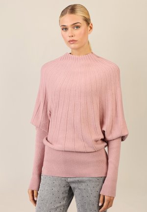 Helles rosa, geripptes Sweater mit hohem Kragen, weit geschnittenen Ärmeln und eng anliegendem Saum. Kombiniert mit grauen Jeans, die kleine dekorative Nieten haben.